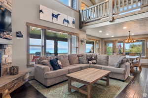 Living area featuring a stone fireplace, hardwood / wood-style flooring, a chandelier, and a high ceiling