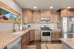 Kitchen featuring stainless steel appliances, light stone counters, dark wood-style floors, recessed lighting, and a textured ceiling