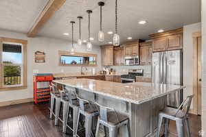 Kitchen with stainless steel appliances, a textured ceiling, dark wood-type flooring, light stone countertops, and a breakfast bar