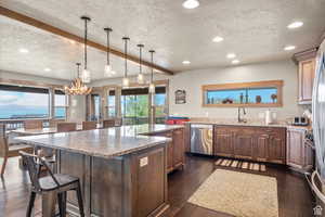 Kitchen with a textured ceiling, light stone counters, dark wood-style floors, a breakfast bar area, and stainless steel appliances