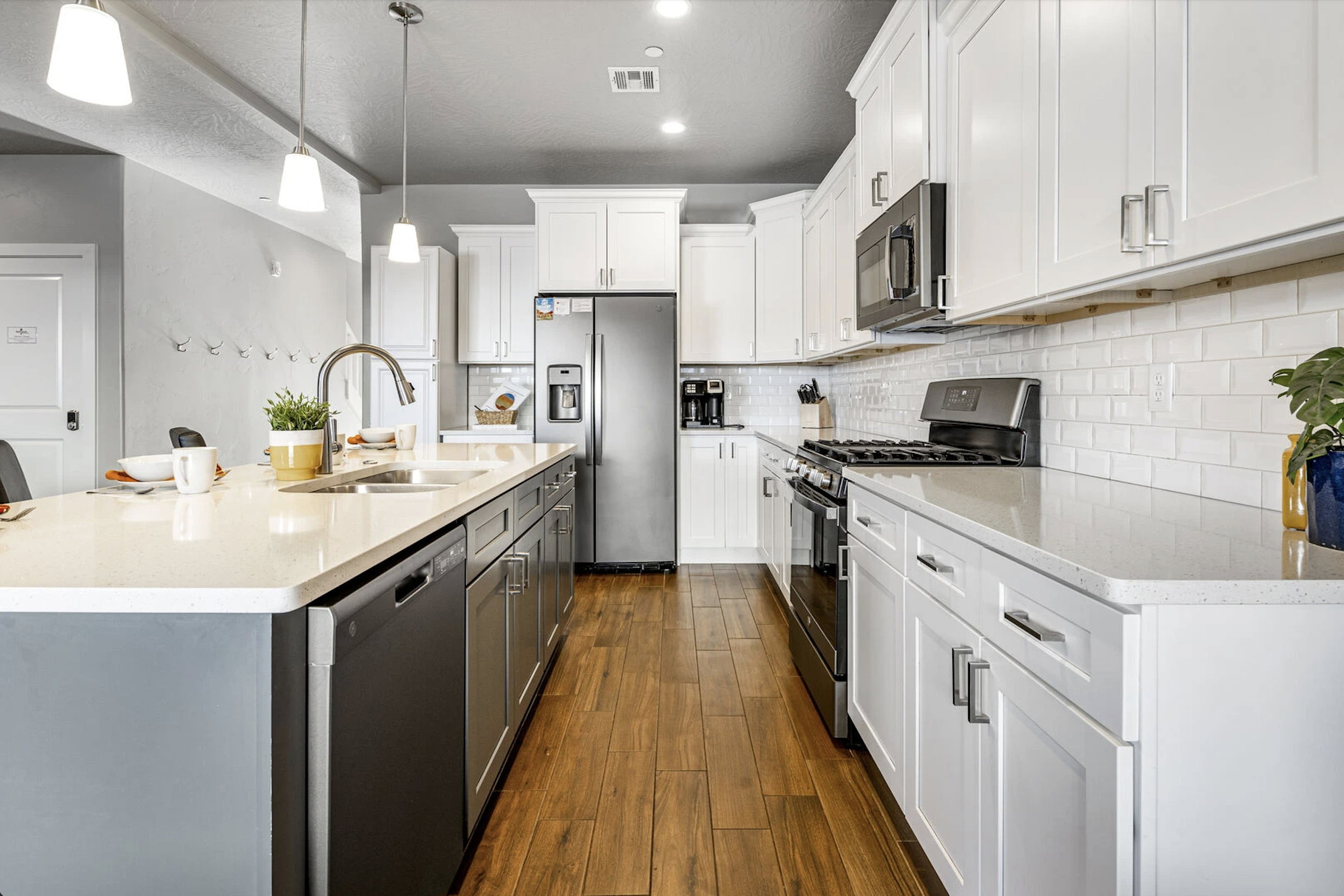 Kitchen with two tone cabinetry, stainless steel appliances, light stone countertops, a center island with sink, and dark wood-type flooring