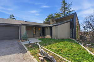 View of front facade with a front lawn, an attached garage, a chimney, a shingled roof, and asphalt driveway