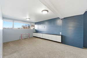 Spare room featuring beamed ceiling, carpet flooring, and wood walls