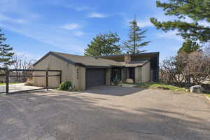 View of front of property featuring an attached garage, driveway, a shingled roof, and a chimney