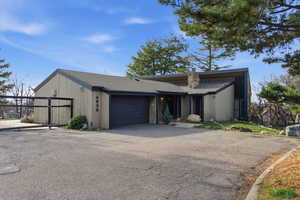 Mid-century inspired home with a chimney, an attached garage, driveway, and roof with shingles