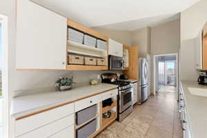 Kitchen with stainless steel appliances, white cabinets, a high ceiling, light tile patterned flooring, and light stone counters