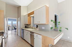 Kitchen featuring a high ceiling, light countertops, light tile patterned floors, stainless steel appliances, and light wood finish cabinets