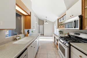 Kitchen with stainless steel appliances, white cabinetry, vaulted ceiling, light countertops, and suspended lighting