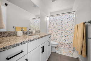 Bathroom featuring a textured ceiling, vanity, curtained shower, and dark tile patterned floors