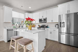 Kitchen featuring stainless steel appliances, white cabinetry, light stone counters, dark wood-type flooring, and a kitchen breakfast bar