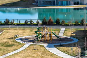 Neighborhood playground featuring a lawn, walking path, and a lake view