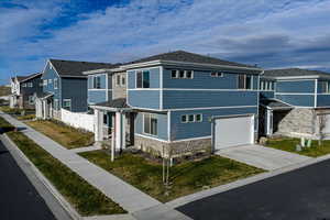 View of front facade featuring a garage, a residential view, stone siding, and concrete driveway