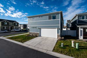 View of front of property with stone siding, a residential view, driveway, an attached garage, and a front yard