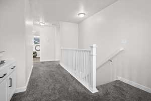 Corridor featuring dark colored carpet, a textured ceiling, and an upstairs landing