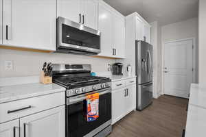 Kitchen featuring stainless steel appliances, white cabinets, light stone countertops, and dark wood-type flooring