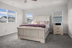 Primary bedroom with dark colored carpet and ceiling fan