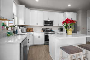 Kitchen with stainless steel appliances, white cabinetry, light stone countertops, light wood-style flooring, and a breakfast bar area