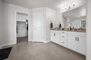 Primary bath with double vanity, a shower, a walk in closet, and a textured ceiling