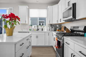 Kitchen with stainless steel appliances, white cabinetry, light stone countertops, light wood-type flooring, and plenty of natural light