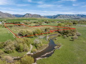Expansive parcel featuring a winding creek, mature trees, open grassy areas, and distant mountains