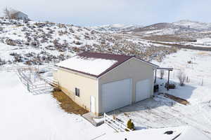 Snow covered property featuring a metal roof, an outdoor structure, a detached garage, and a mountain view