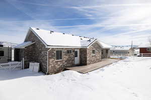 Snow covered rear of property featuring a deck and brick siding