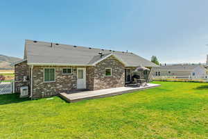 Rear view of house featuring brick siding, roof with shingles, and a patio