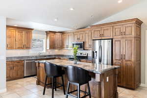 Kitchen featuring stainless steel appliances, dark stone countertops, a kitchen breakfast bar, wood finish cabinetry, and recessed lighting