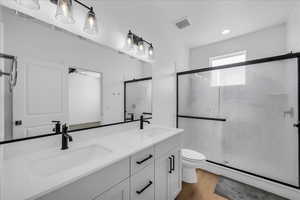 Full bathroom with double vanity, a shower stall, light wood-style flooring, and recessed lighting