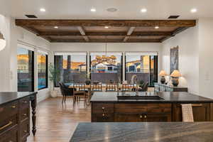Kitchen featuring dark wood finish cabinets, a chandelier, light wood-style flooring, dark stone counters, and beam ceiling