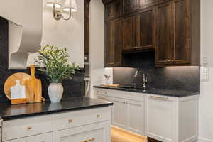 Kitchen featuring backsplash, dark stone countertops, light wood-type flooring, pendant lighting, and dark wood finish cabinetry
