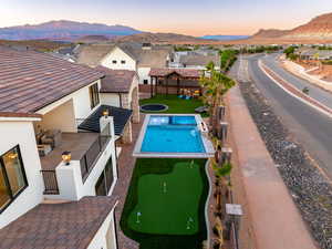 Pool at dusk with a patio, a mountain view, an area to practice putting, and a pergola