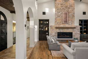 Living area with arched walkways, a high ceiling, a stone fireplace, and wood finished floors