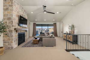 Living room featuring arched walkways, light colored carpet, a ceiling fan, lofted ceiling, and a stone fireplace