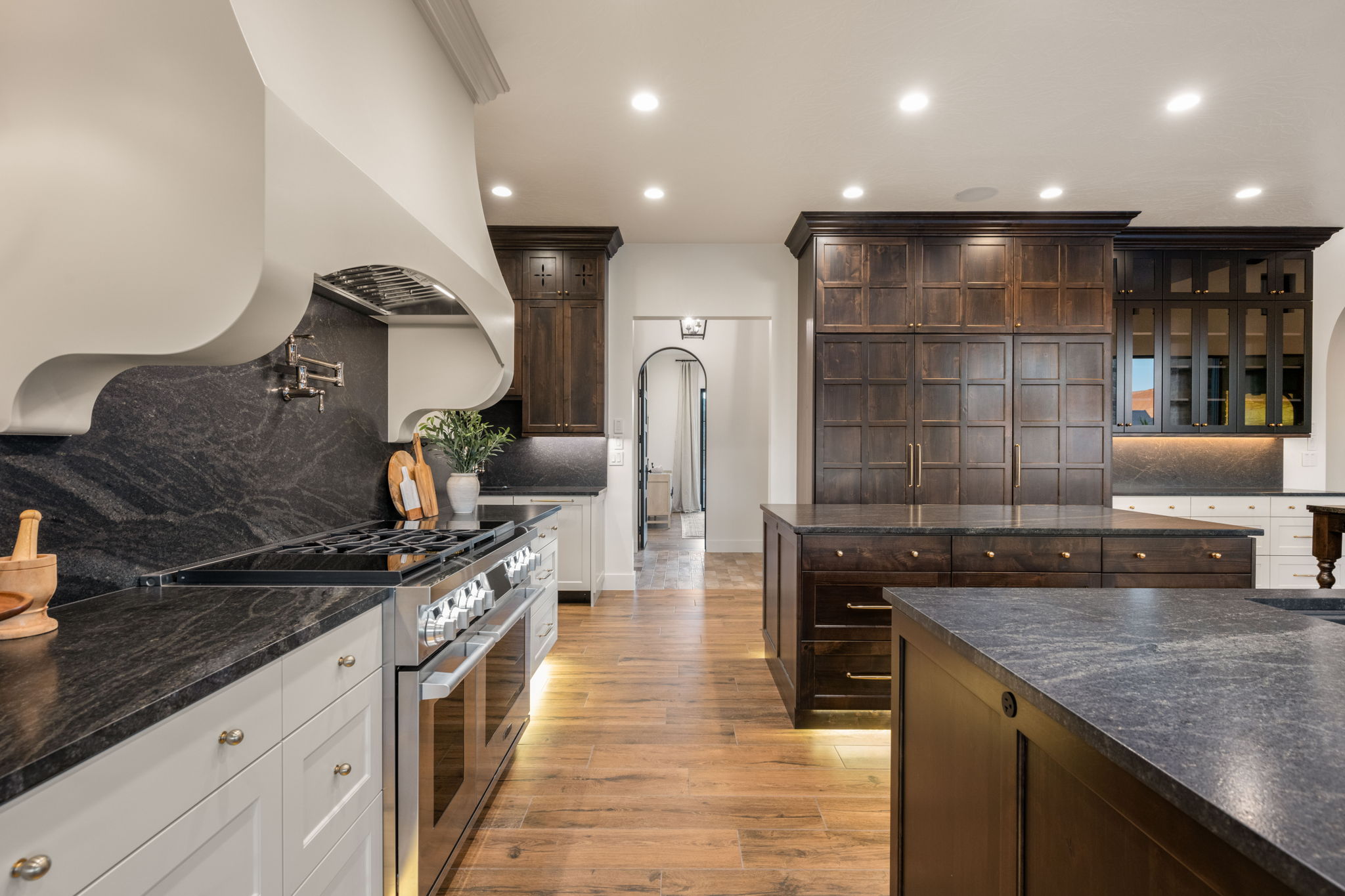 Kitchen featuring backsplash, dark wood finish cabinets, range with two ovens, arched walkways, and recessed lighting
