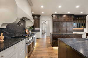 Kitchen featuring backsplash, dark wood finish cabinets, range with two ovens, arched walkways, and recessed lighting