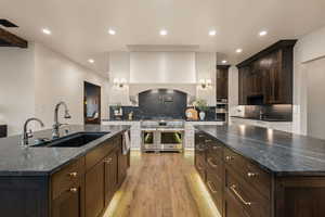 Two tone kitchen featuring a large island with sink, decorative backsplash, stainless steel appliances, dark stone counters, and light wood-style flooring