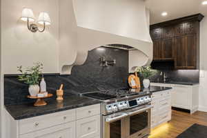 Kitchen with range with two ovens, light wood finished floors, dark stone counters, recessed lighting, and backsplash