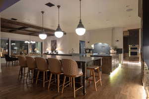 Kitchen featuring dark wood finish cabinetry, dark wood-type flooring, hanging light fixtures, a breakfast bar, and stainless steel double oven