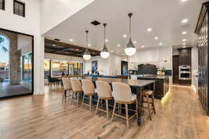 Kitchen with dark wood finish cabinetry, hanging light fixtures, a breakfast bar area, light wood-style flooring, and decorative backsplash