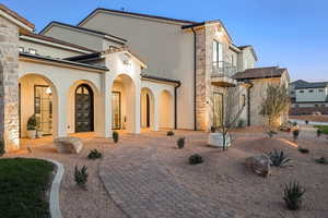 Rear view of property featuring stucco siding, stone siding, and a balcony