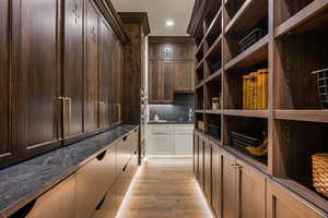 Bar featuring tasteful backsplash, light wood-style flooring, dark stone counters, dual tone cabinetry, and recessed lighting