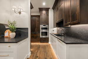 Kitchen featuring recessed lighting, double oven, dark stone counters, light wood-type flooring, and tasteful backsplash