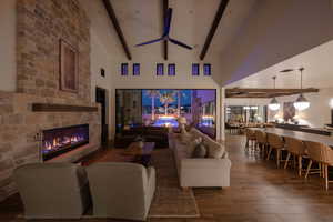 Living area with dark wood finished floors, a stone fireplace, a ceiling fan, and lofted ceiling
