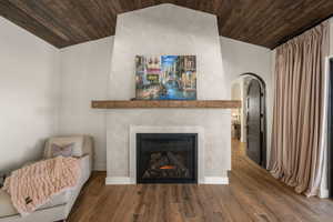 Living room featuring arched walkways, wooden ceiling, dark wood-style flooring, and a tile fireplace