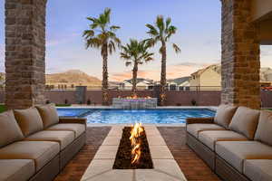 View of pool featuring an outdoor living space with a fire pit, patio surround, and a fenced backyard