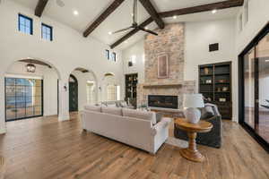 Living area with arched walkways, hardwood / wood-style floors, built in features, a ceiling fan, and a stone fireplace