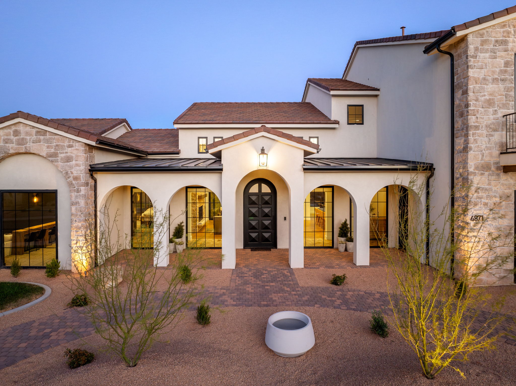 View of front facade with stone siding, a standing seam roof, stucco siding, and driveway