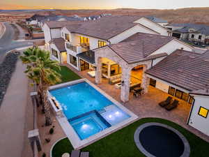 Pool at dusk with a patio, a pool with connected hot tub, outdoor furniture, a residential view, and a yard