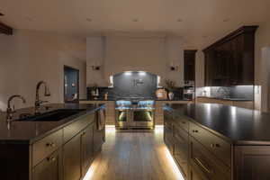 Kitchen with dark wood finish cabinets, a center island with sink, decorative backsplash, and stainless steel appliances